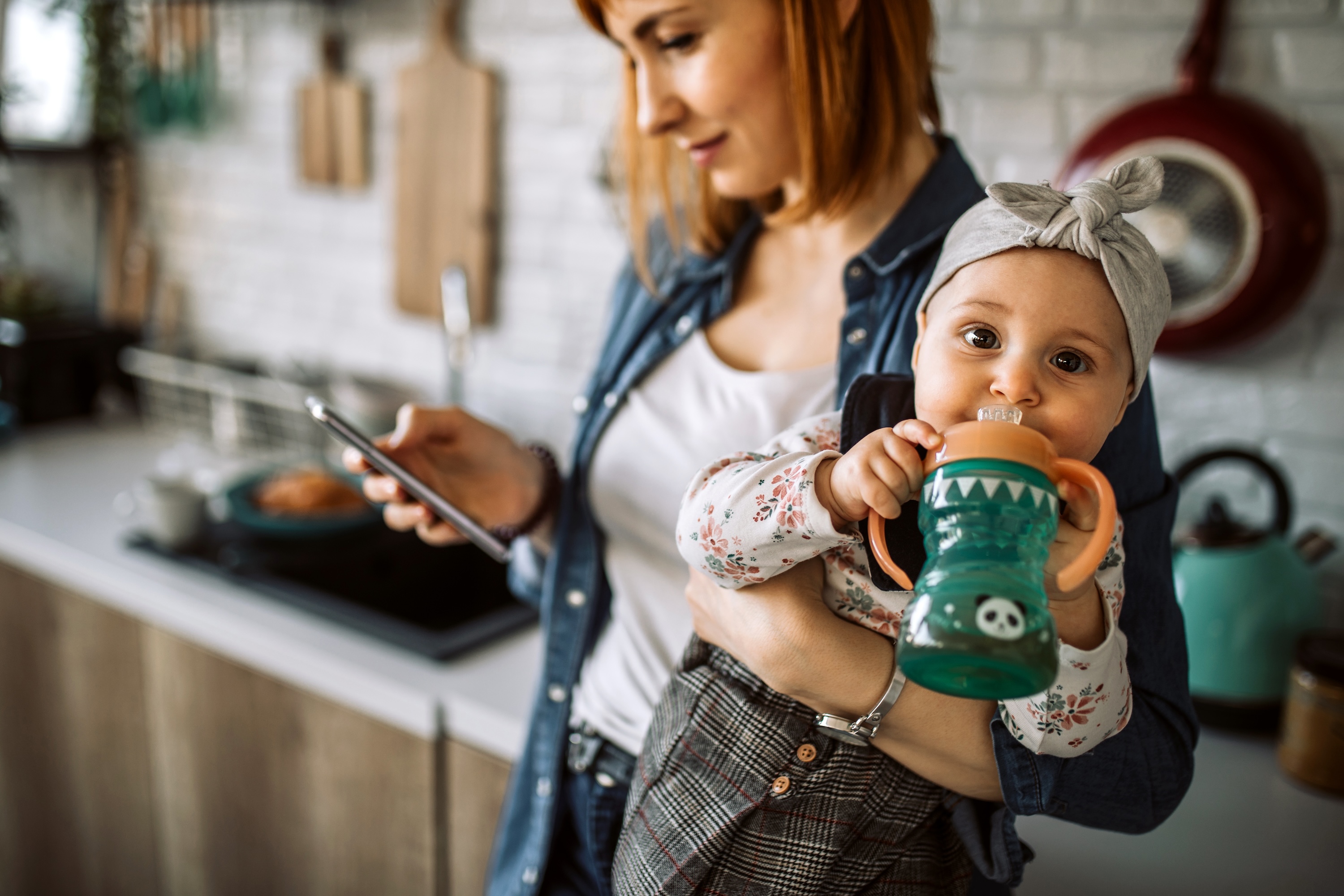 young woman carrying her cute baby girl while using smart phone