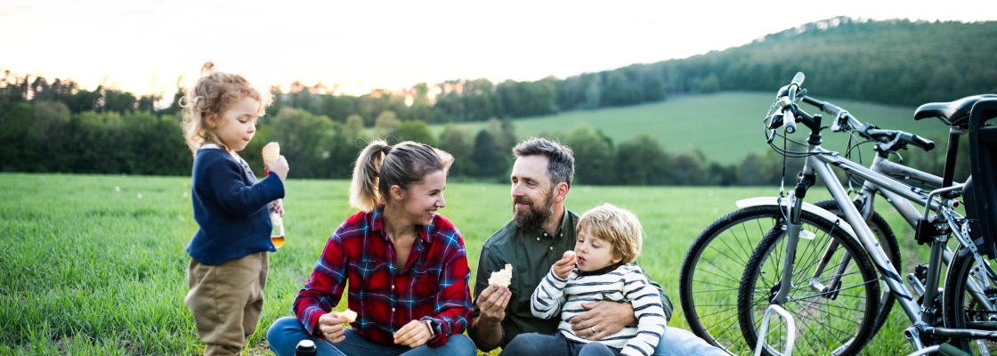 family with two small children on cycling trip sitting on grass and resting