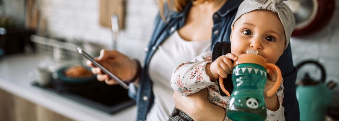 young woman carrying her cute baby girl while using smart phone