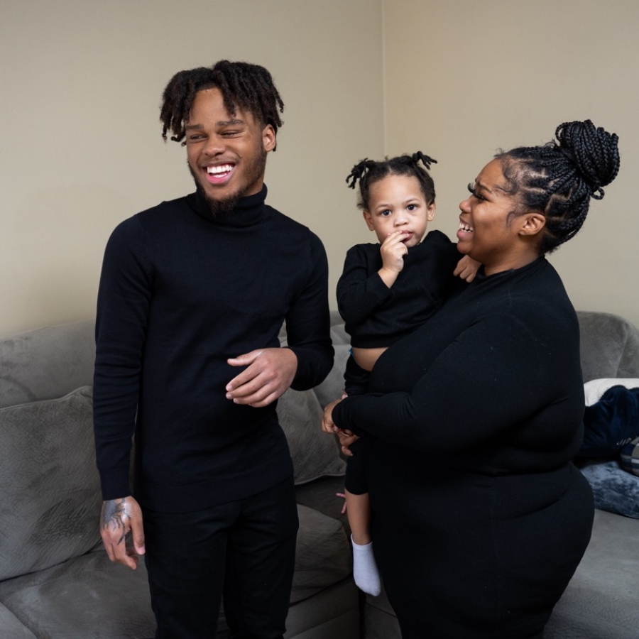 a family of three stand together in a living room laughing